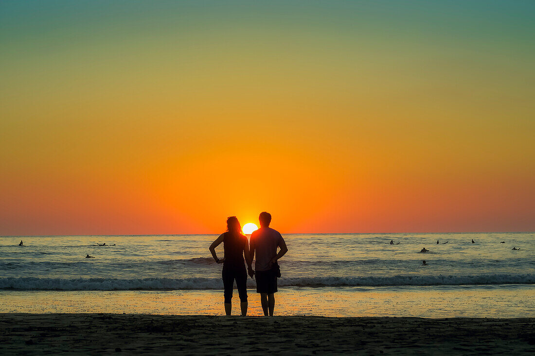 Paar hält sich an der Hand am Guiones Strand, wo sich die Leute zum Surfen und Beobachten des Sonnenuntergangs versammeln, Playa Guiones, Nosara, Guanacaste, Costa Rica, Mittelamerika