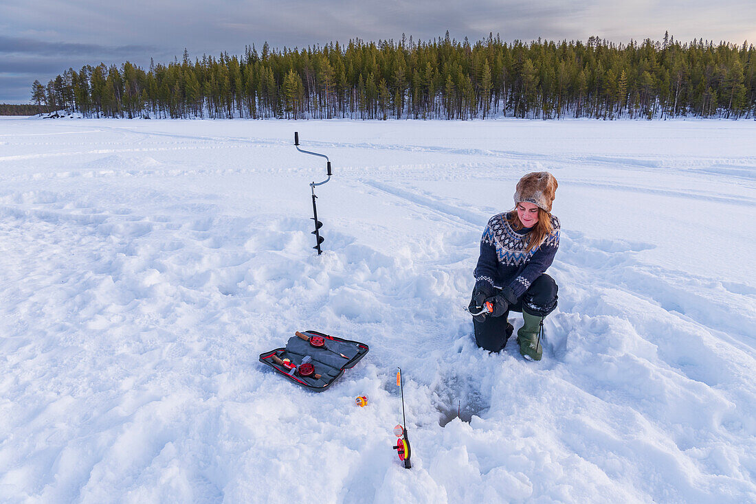 Woman in Scandinavian clothes ice fishing on a frozen lake, Lapland, Sweden, Scandinavia, Europe