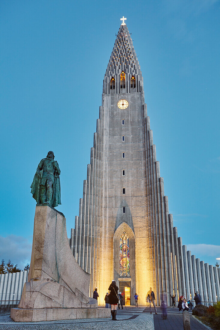 Ein Blick in der Abenddämmerung auf den Kirchturm der Hallgrimskirkja Kirche, vor der eine Statue von Leifur Eriksson, dem Gründer Islands, steht, im Zentrum von Reykjavik, Island, Polarregionen
