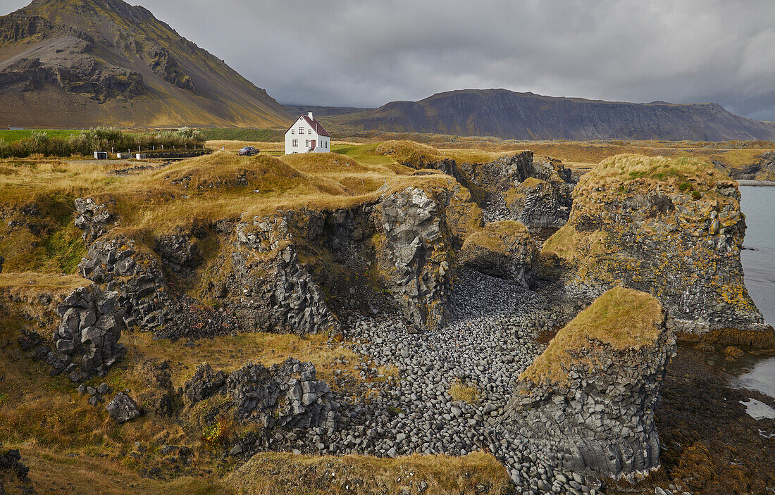 A classic view of the basalt lava cliffs on the coast at the village of Arnastapi, backed by the mountains of Snaefellsjokull, Snaefellsjokull National Park, Snaefellsness peninsula, west coast of Iceland, Polar Regions