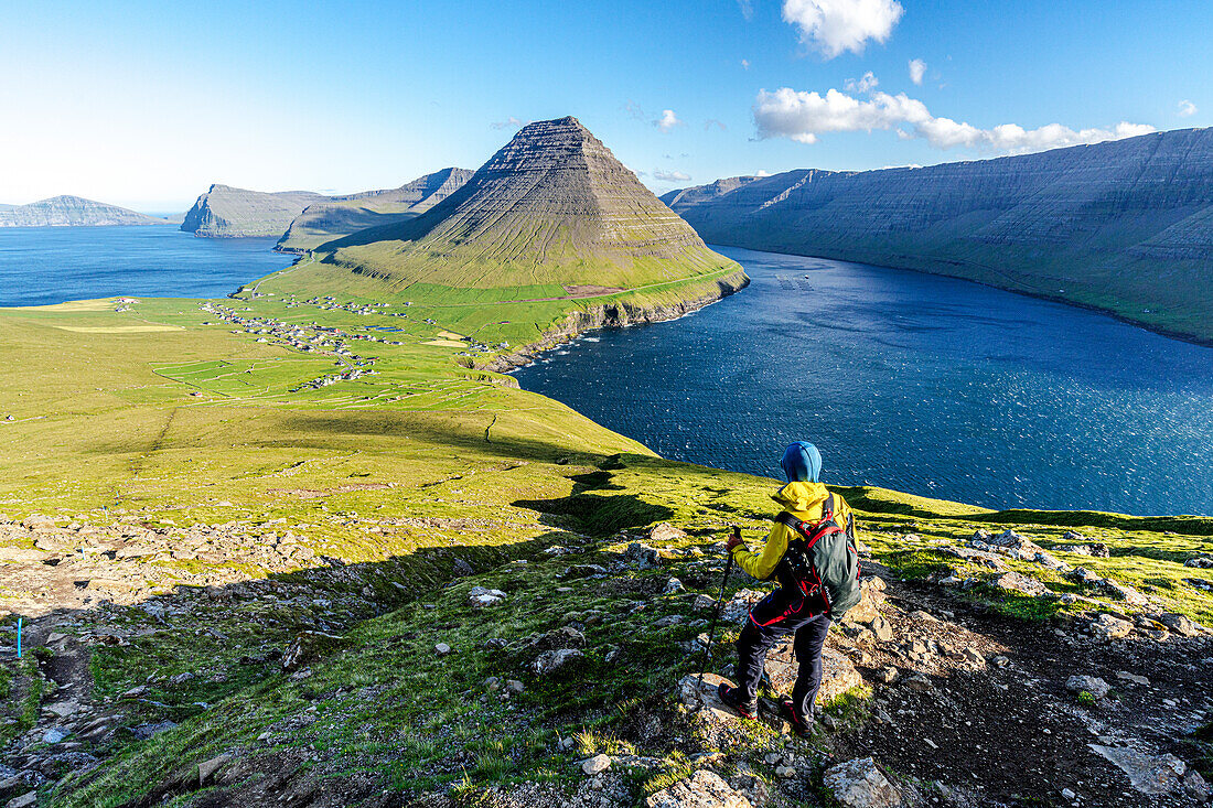 Wanderer steht auf dem Gipfel eines Hügels mit dem Dorf Vidareidi und dem Berg Malinsfjall im Hintergrund, Insel Vidoy, Färöer, Dänemark, Europa