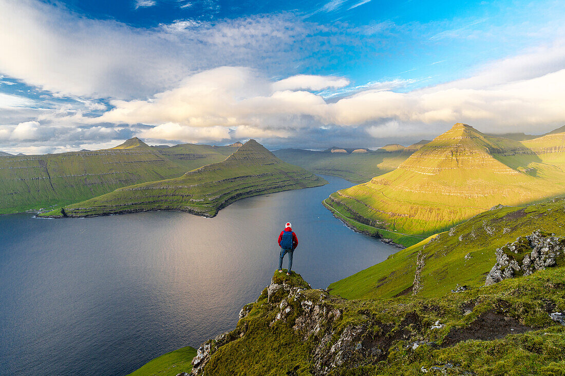Hiker with backpack enjoying the view standing on rocks overlooking Funningur fjord, Eysturoy Island, Faroe Islands, Denmark, Europe
