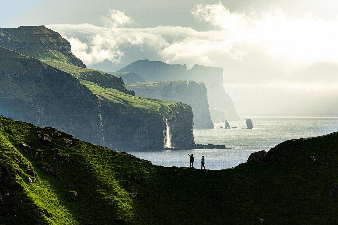 Silhouette von Wanderern, die auf einem Bergkamm über dem Meer stehen und die Klippen bewundern, Insel Kalsoy, Färöer, Dänemark, Europa