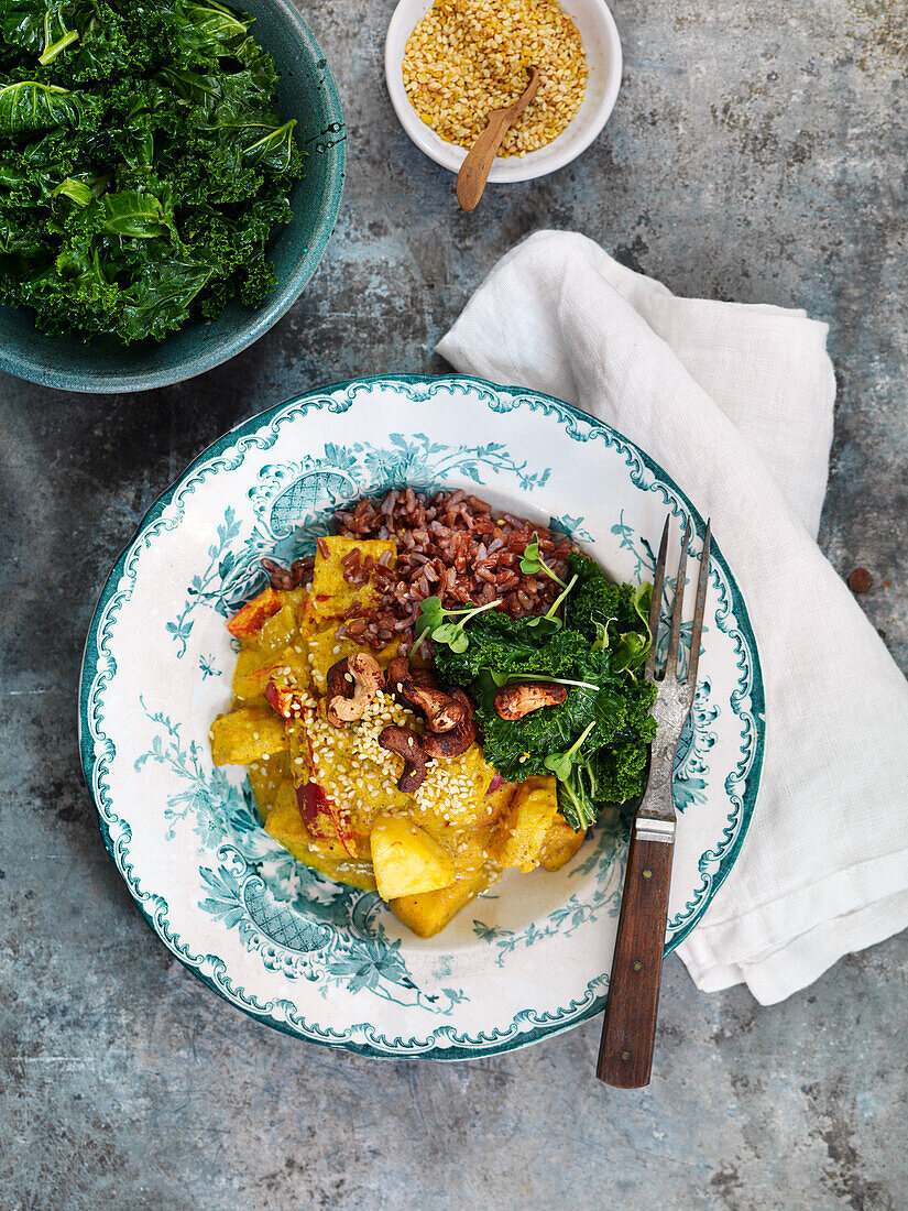 Vegan stew with curry, red bell pepper, cashew nuts, kale, and red rice