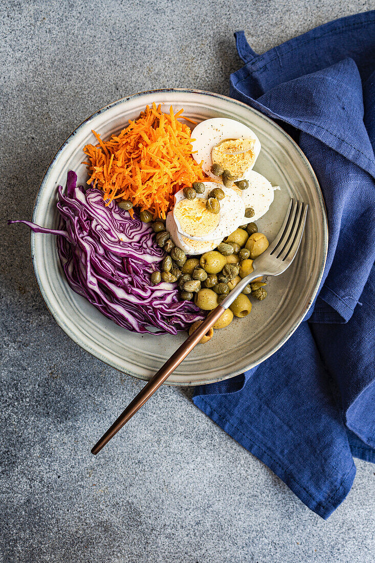 Bowl with boiled eggs, capers, olives, red cabbage and carrots (keto cuisine)