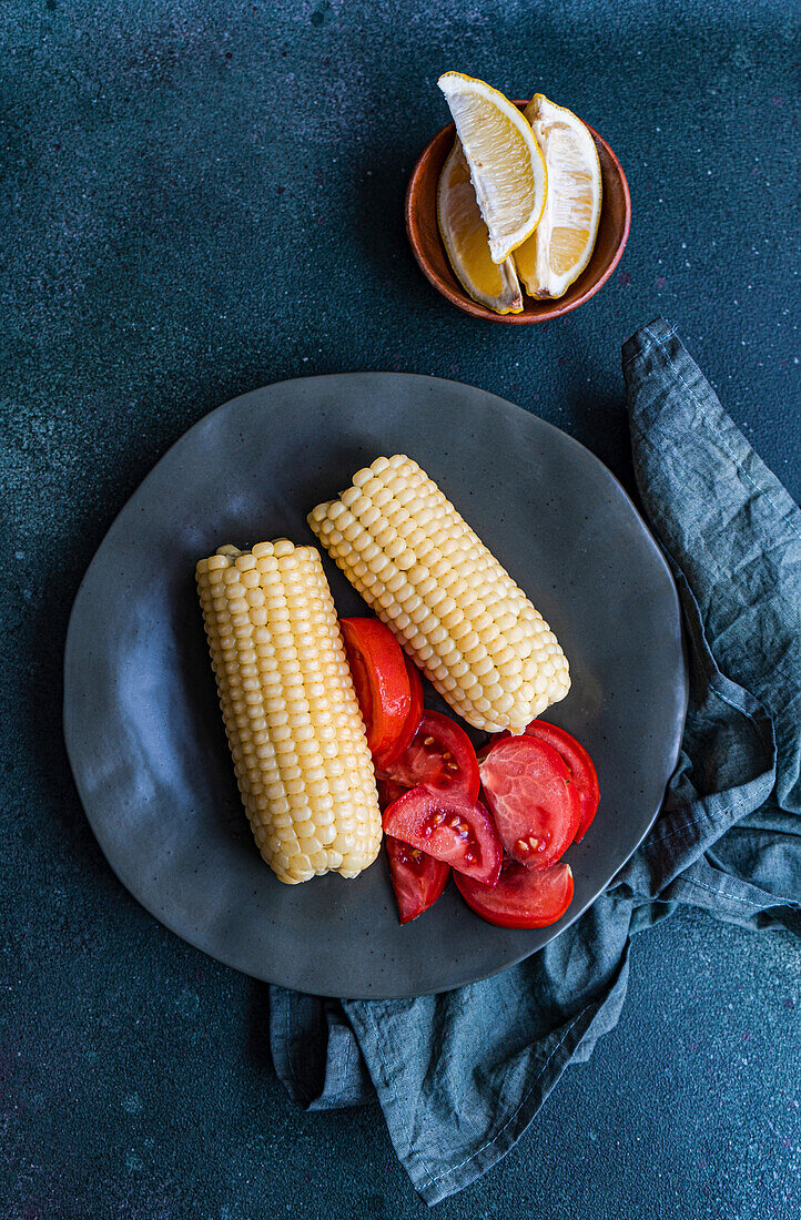 Gekochte weiße Maiskolben mit Tomaten