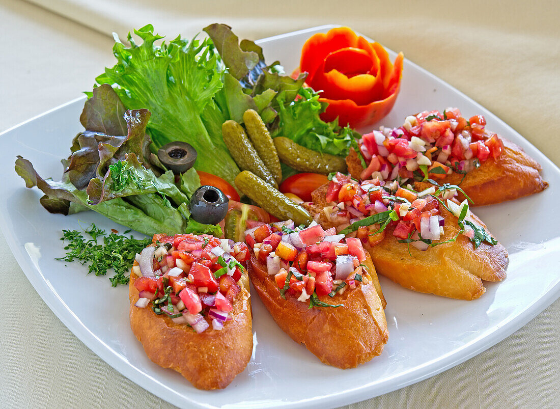 Baguettescheiben mit Tomatensalsa, garniert mit grünem Salat, Cornichons und Oliven