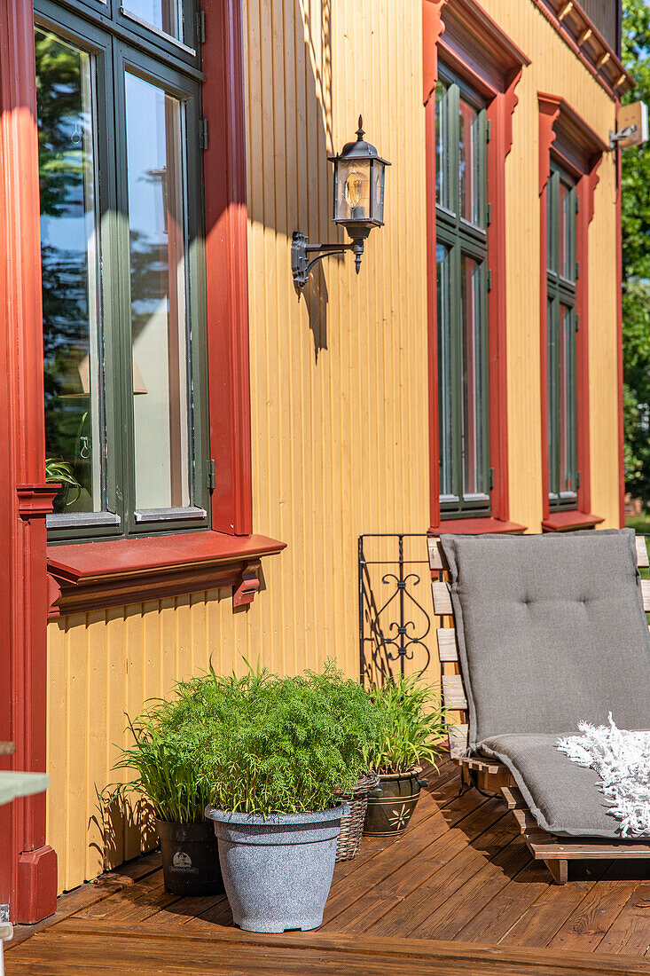 Veranda mit Liegestuhl und Topfpflanzen, gelbe Holzfassade
