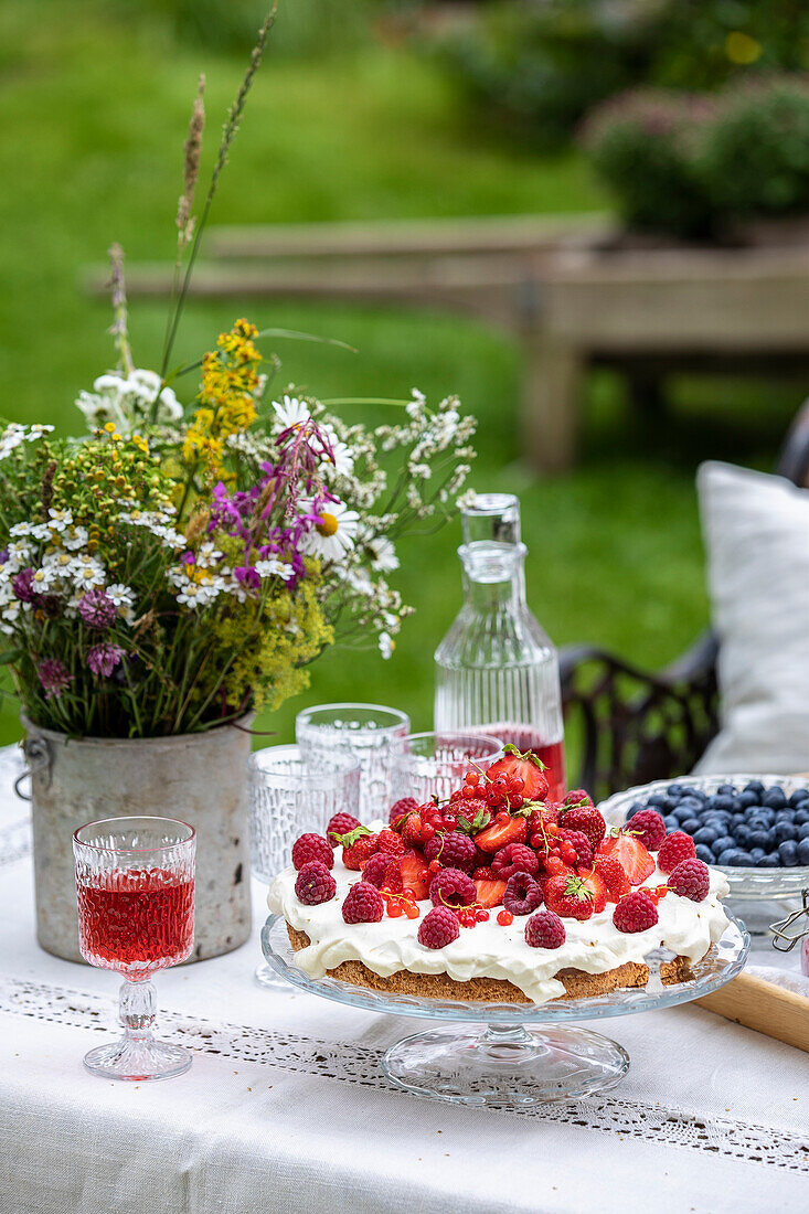 Sommerliches Picknick mit Beerentorte und Wildblumenstrauß im Garten