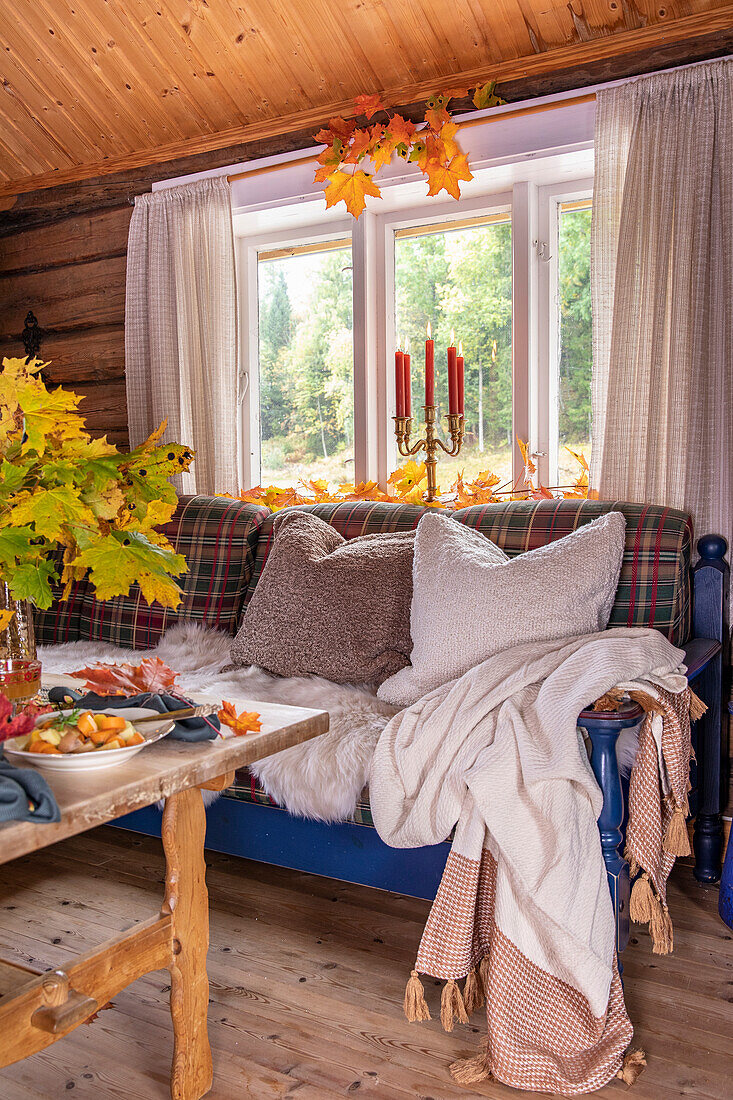 Autumnally decorated window sill and cosy sofa in a wooden hut