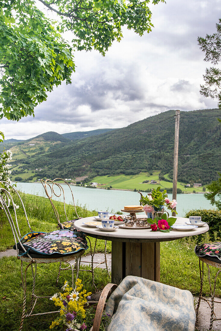 Idyllisches Gartenfrühstück am Holztisch mit Bergblick und Seepanorama