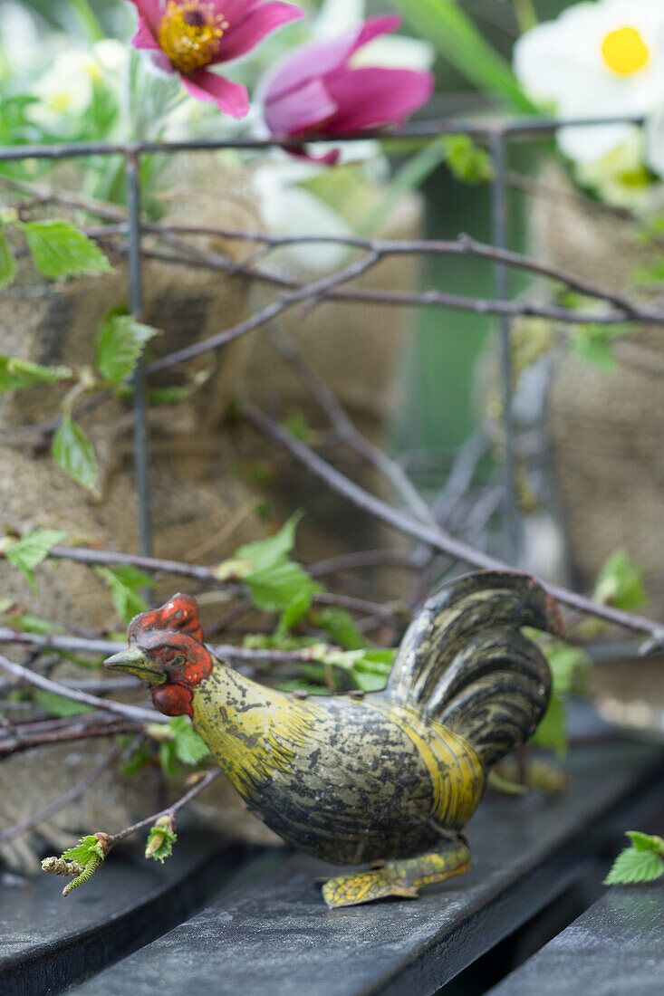 Birch twigs and rooster figurine, in the background a pasque flower (Pulsatilla) and daffodils (Narcissus)