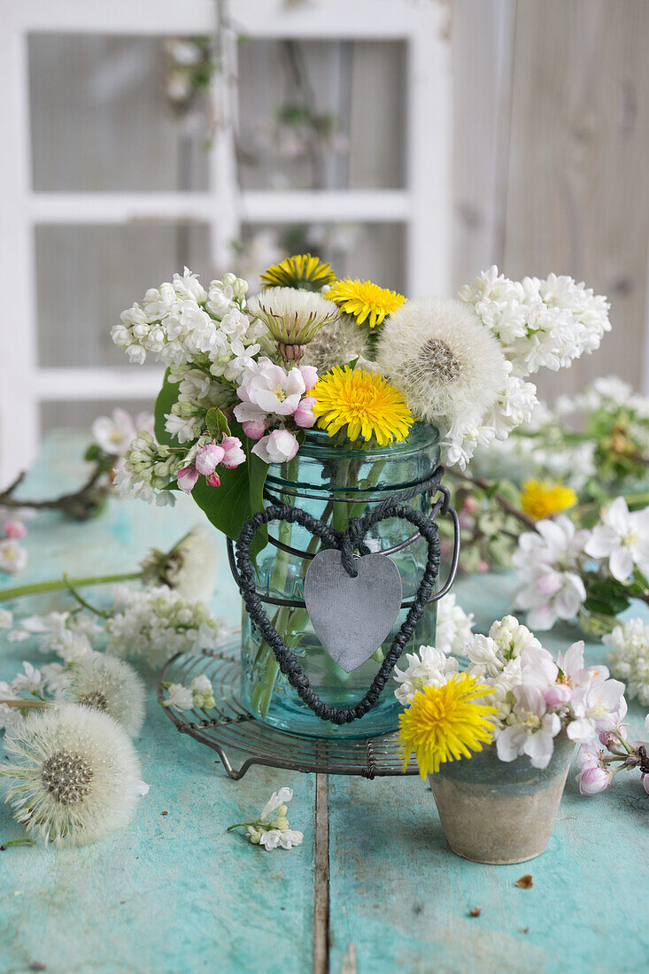 Strauß aus Apfelblüten, Fliederblüten (Syringa) und Löwenzahn (Taraxum) im Bügelglas, mit Herzen aus Schnur und Blech