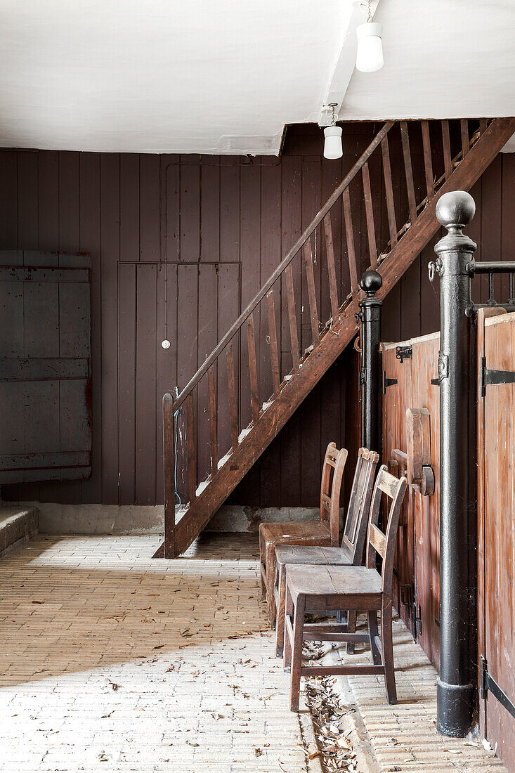 Old wooden staircase and wooden chairs in a stable with a brick floor