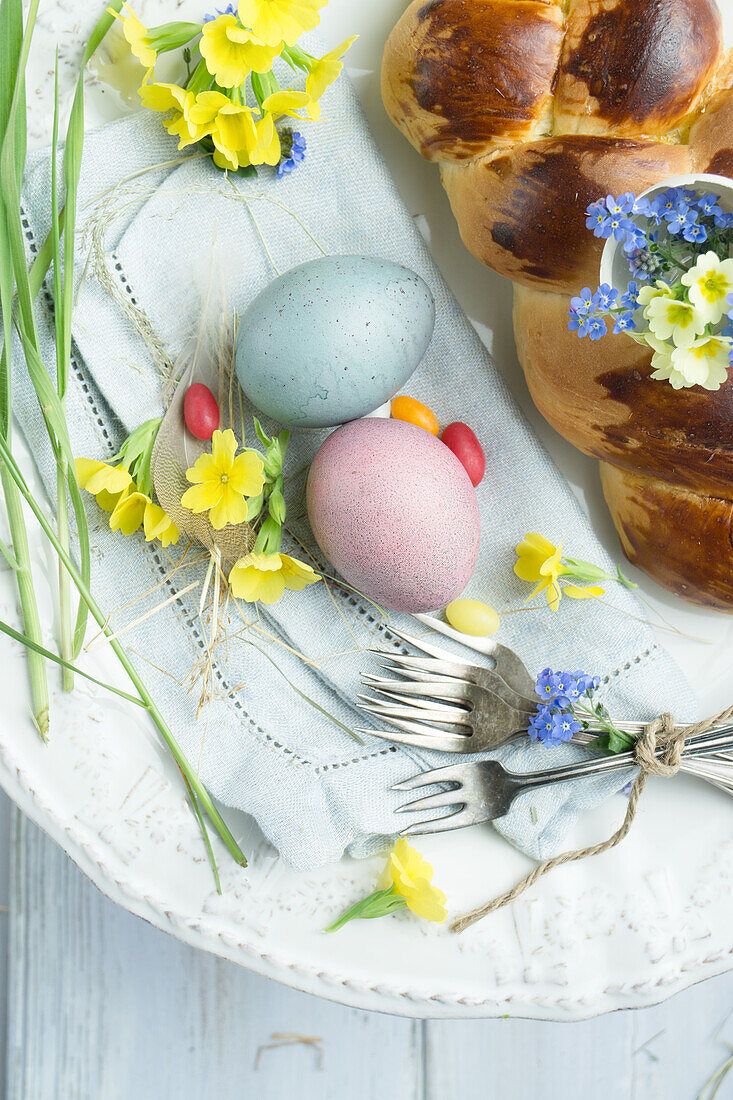 Osterzopf mit eingebackener Eierschale gefüllt mit Schlüsselblumen und Vergissmeinnicht, Ostereier und Besteck auf Serviette