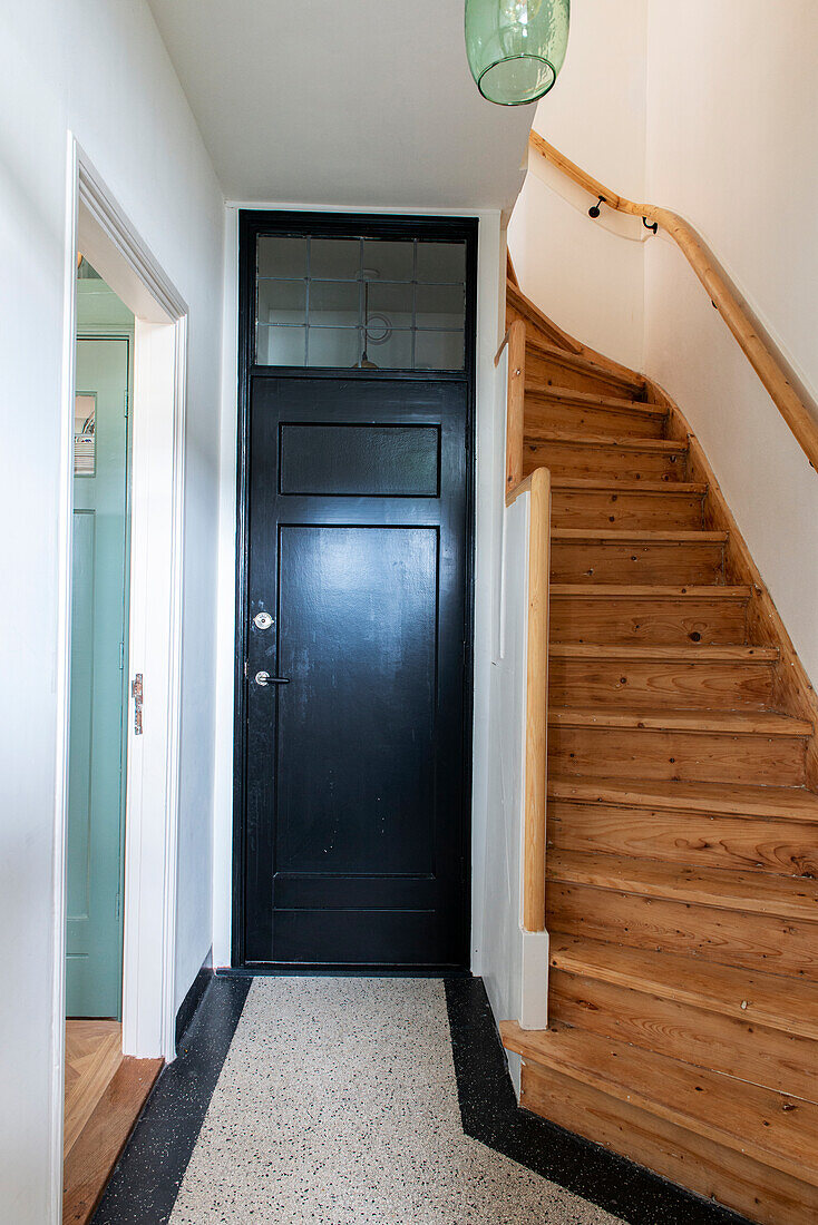 Narrow hallway with wooden staircase and black door