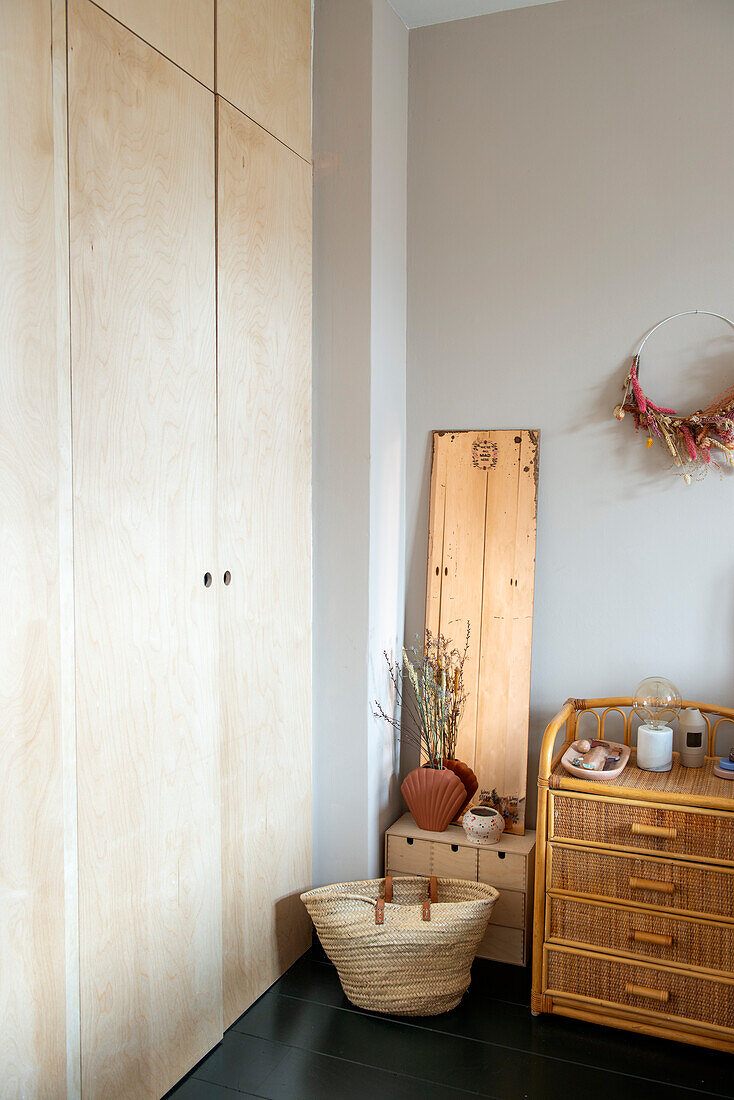 Built-in wardrobe made of light-colored wood, rattan chest of drawers and dried flower decoration