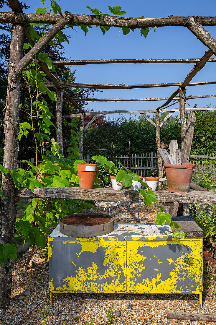 Rustic garden table with peeling yellow paint and flower pots under pergola