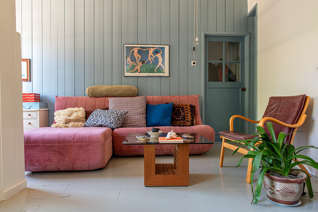 Living room with pink sofa, wooden table and leather armchair in front of blue wall panelling