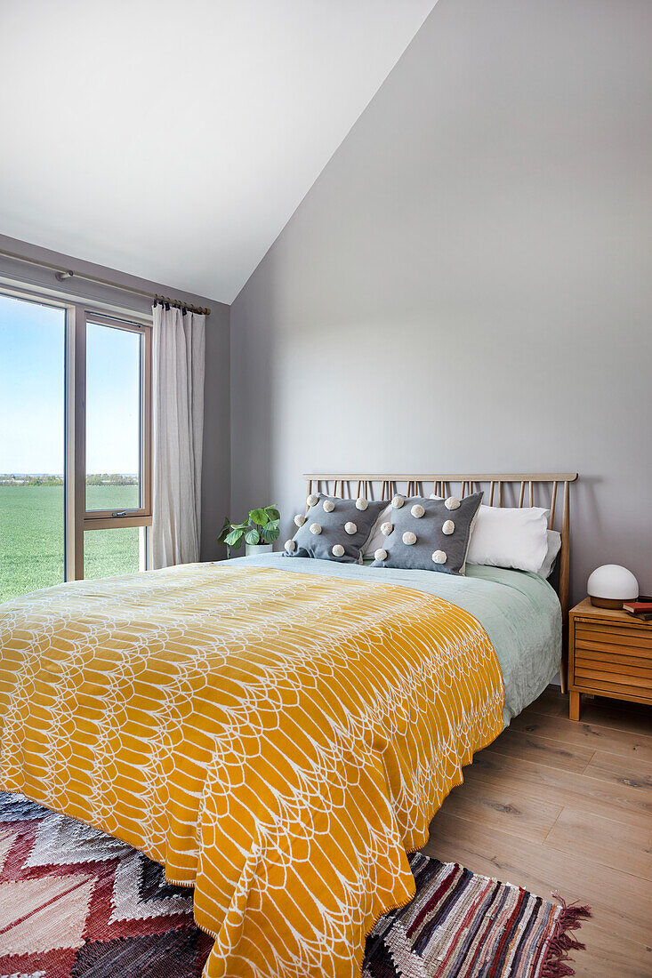 Bed with yellow bedspread, sloping ceiling and patterned carpet in bedroom