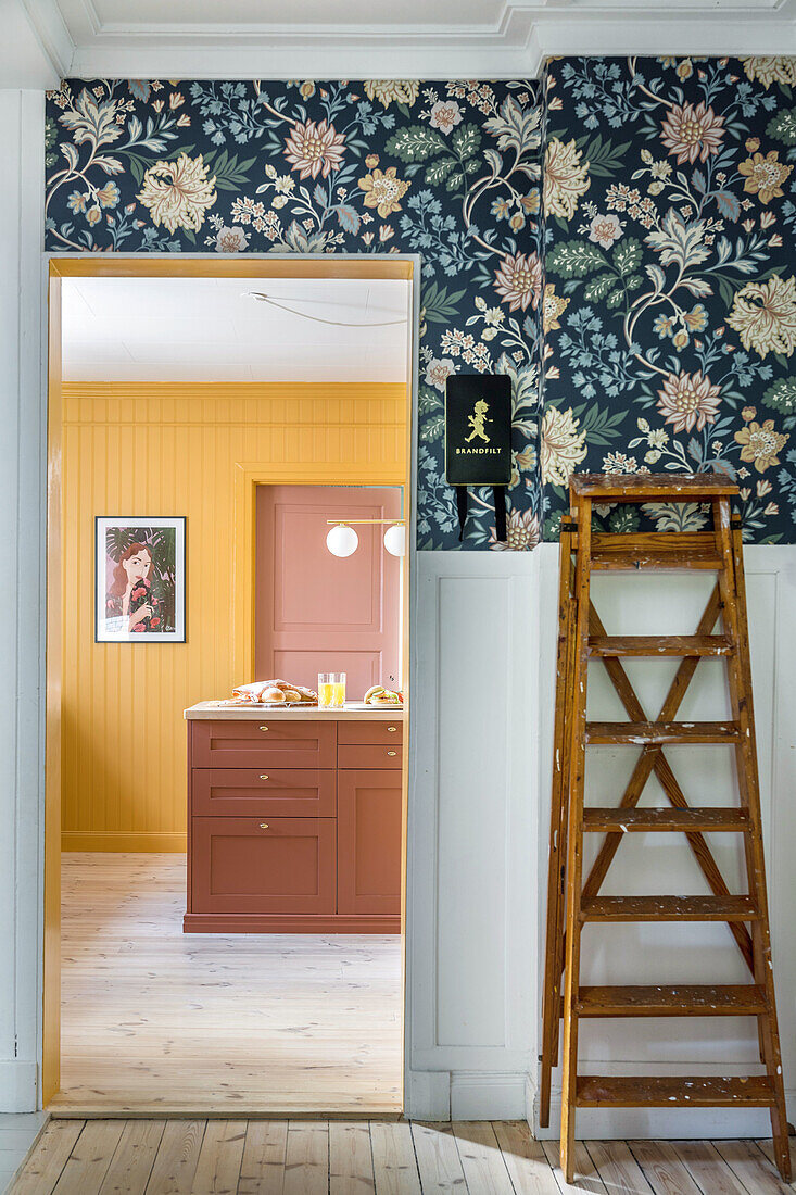 Passageway with floral patterned wallpaper, view of kitchen with yellow walls