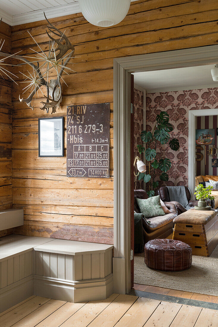 Wood-paneled hallway with view into the living room with wallpaper and leather sofa