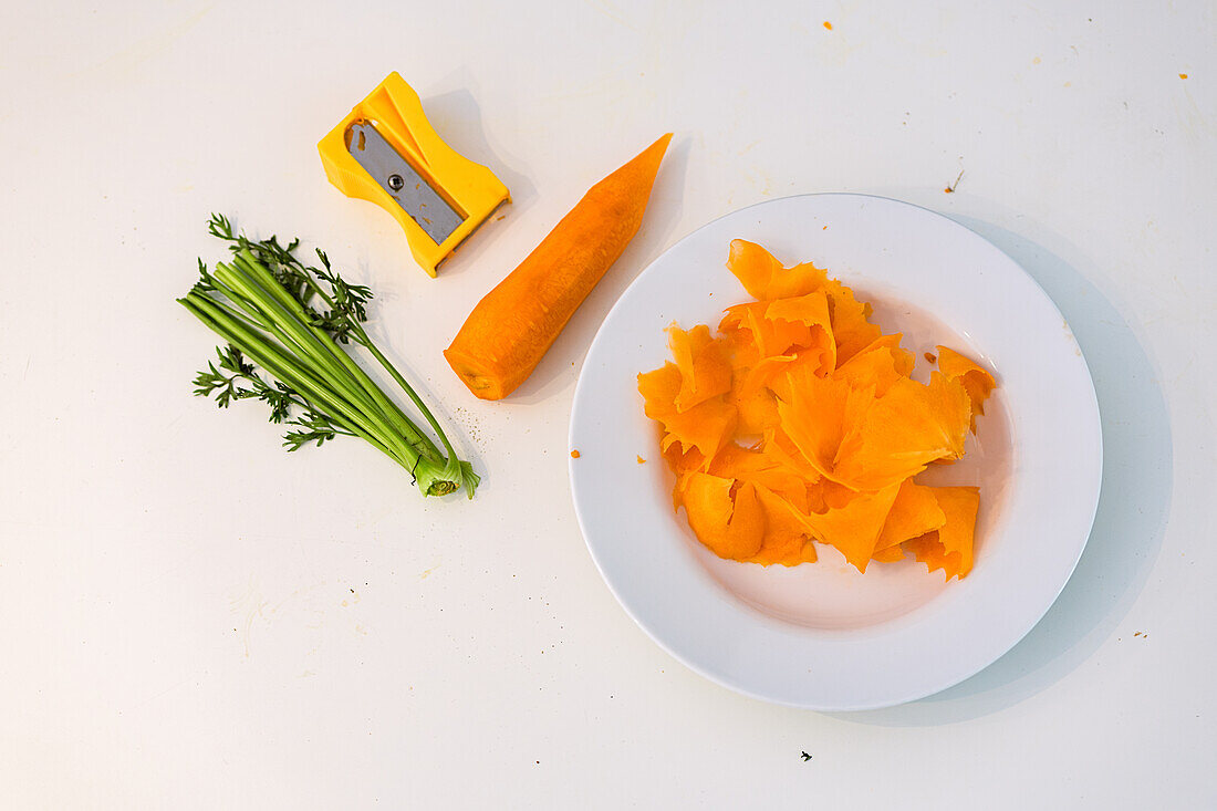 Sliced carrots, peeled carrot, carrot greens and sharpener