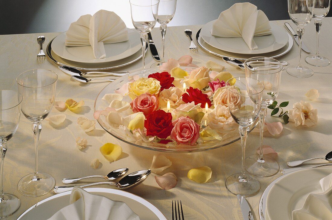 Schale mit Rosenblüten & Kerzen auf festlich gedecktem Tisch