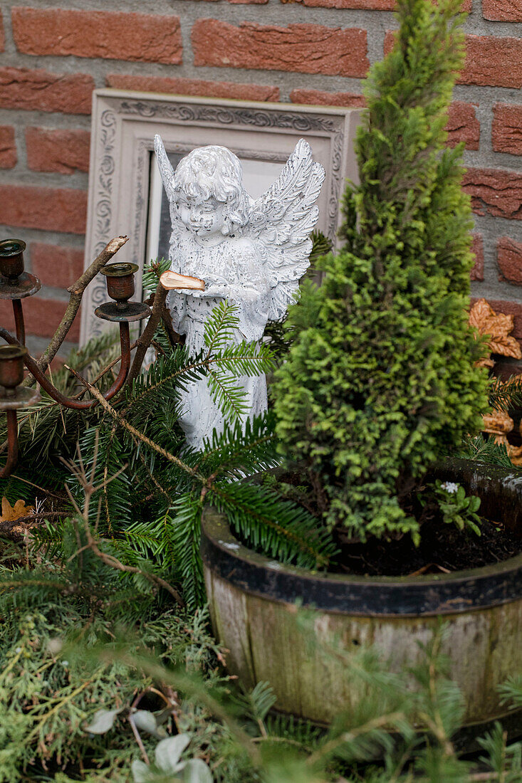 Angel figurine next to thuja in a wooden pot with fir branches and candle holder