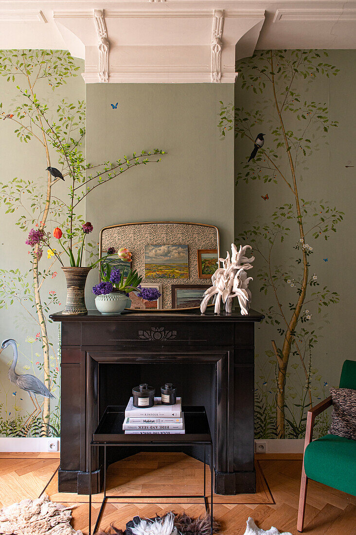 Fireplace with dark wooden frame in front of wallpaper with nature motif