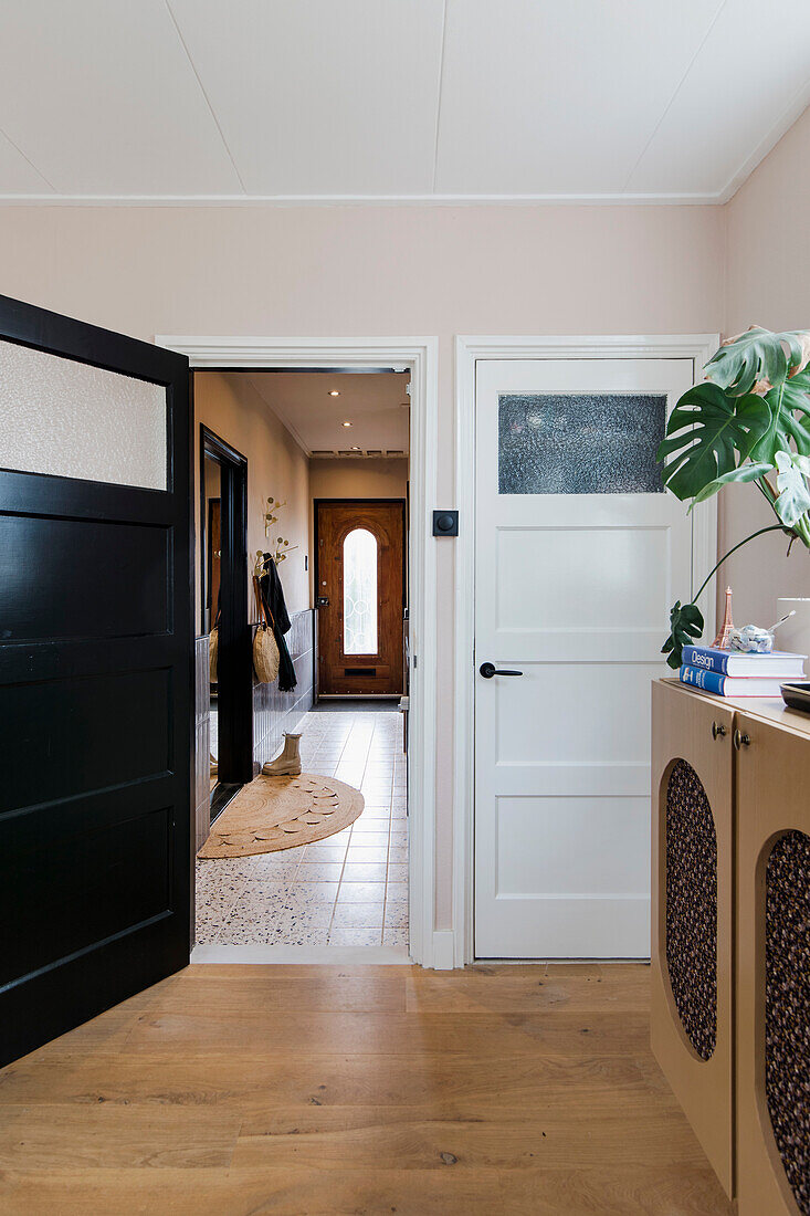 Hallway with wooden floor, white and black doors and monstera plant