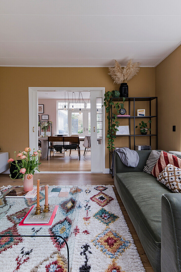 Wohnzimmer mit grünem Sofa, buntem Teppich und Blick ins Esszimmer