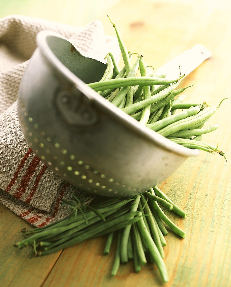 Green beans (French beans) in strainer & beside it on table