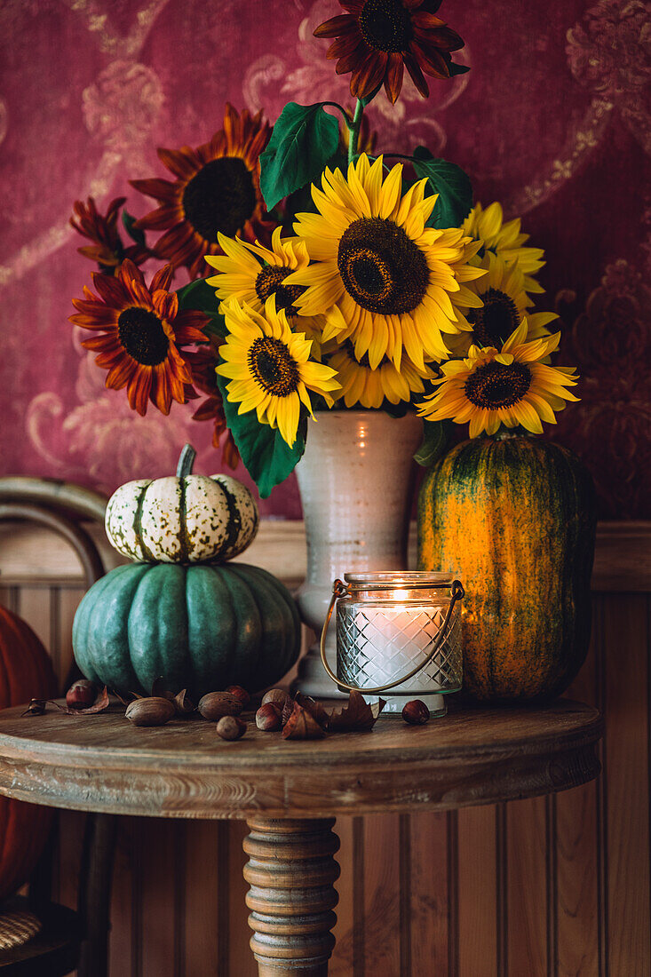 Herbstlicher Blumenstrauß aus Sonnenblumen (Helianthus) und Kürbisse auf rundem Tisch