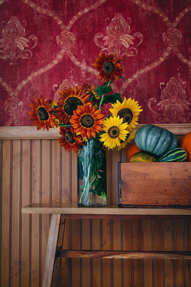 Herbstlicher Blumenstrauß aus Sonnenblumen (Helianthus) und Kürbisse vor alter Tapete