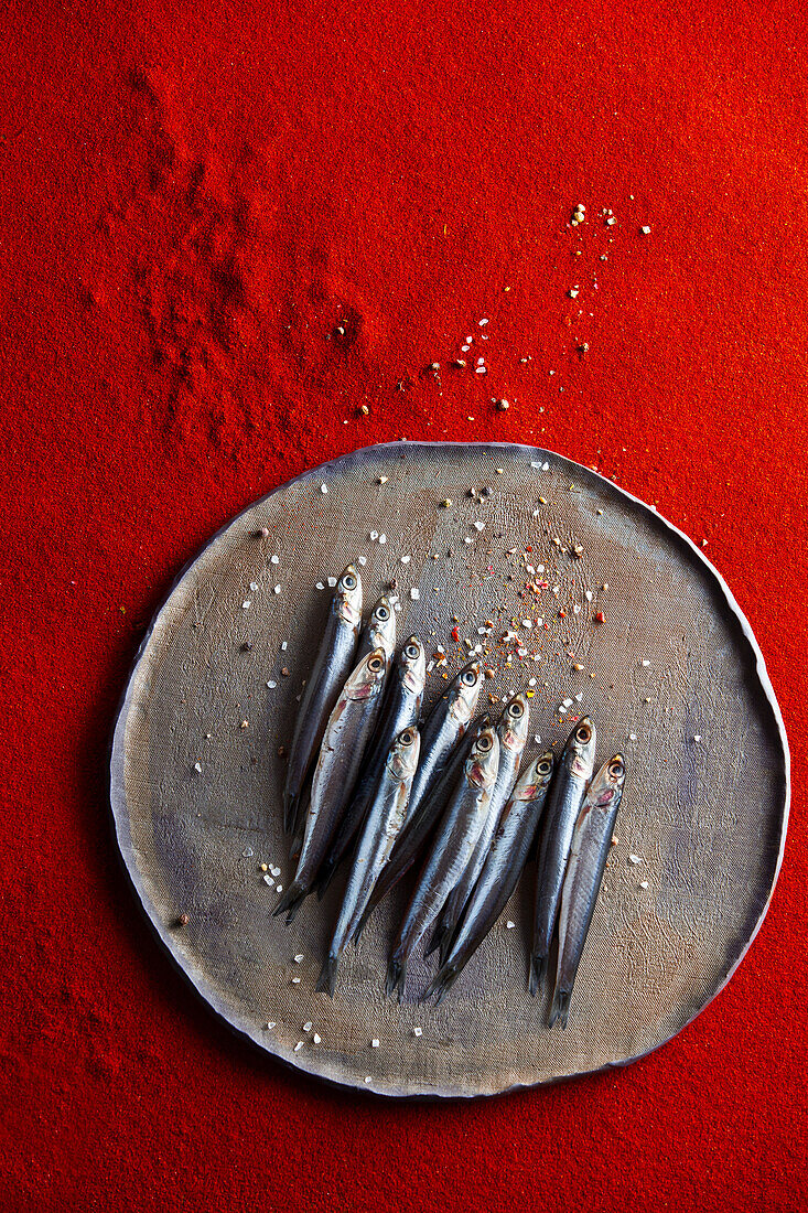 Fresh anchovies on a tray against a red background