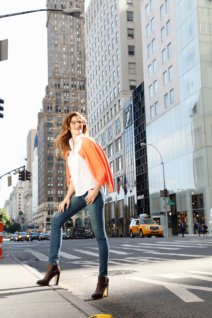 Young woman with glasses stands on the street with skyscrapers