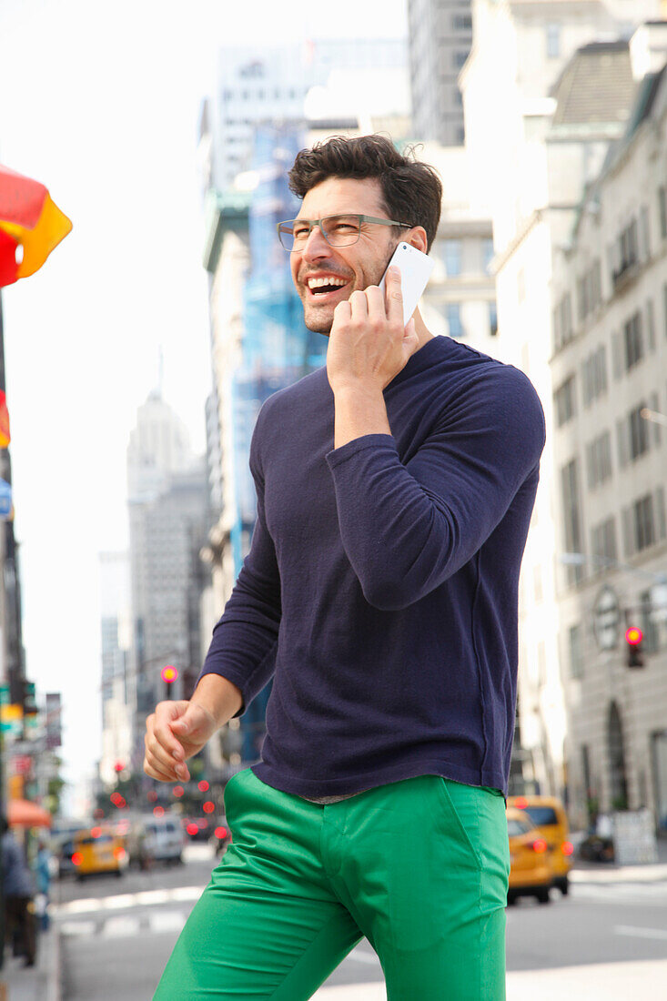 Fröhlicher junger Mann mit Brille im telefoniert auf der Straße