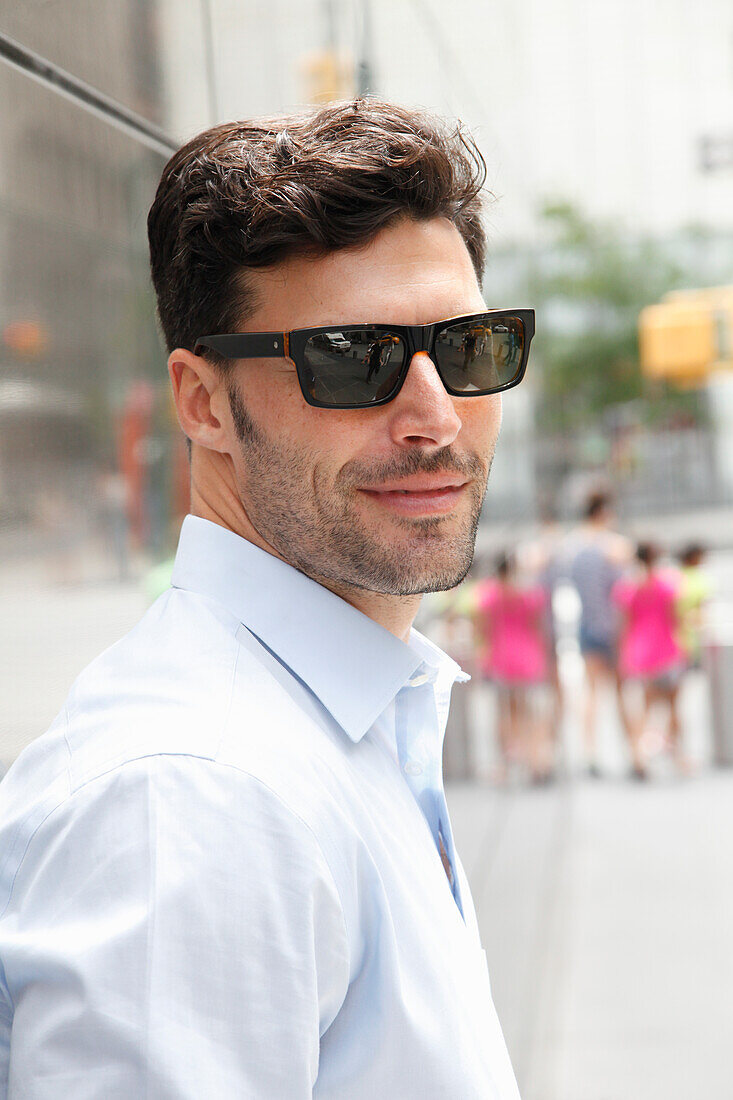 Young man with sunglasses in a light shirt stands on the street