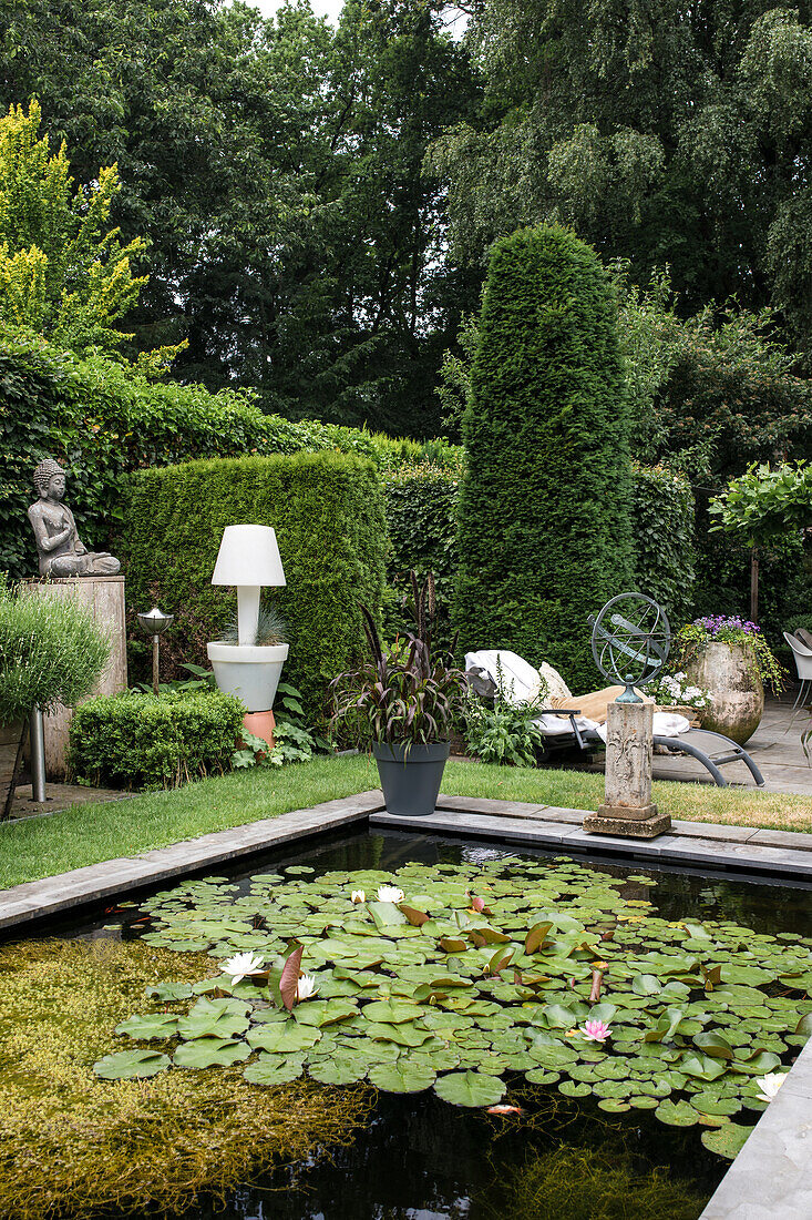 Gepflegter Garten mit Seerosen-Teich, hohen Hecken und Buddha-Statue