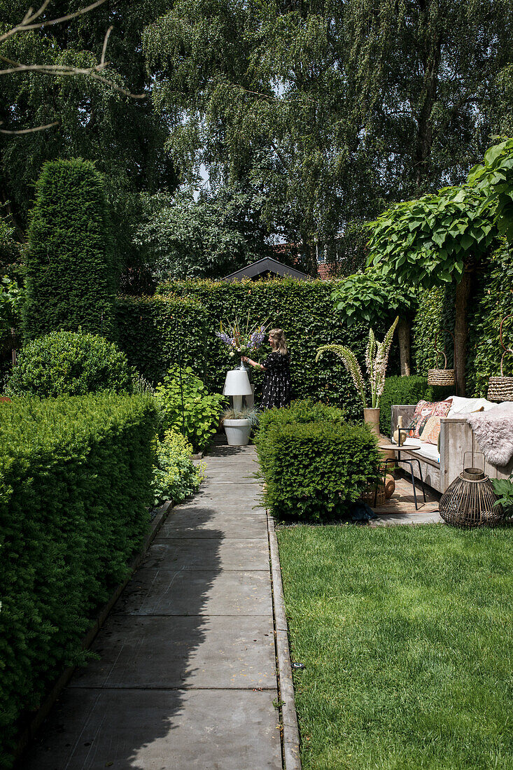 Gepflasterter Gartenpfad mit geschnittenen Hecken, gemütlichem Sitzbereich und gepflegtem Rasen