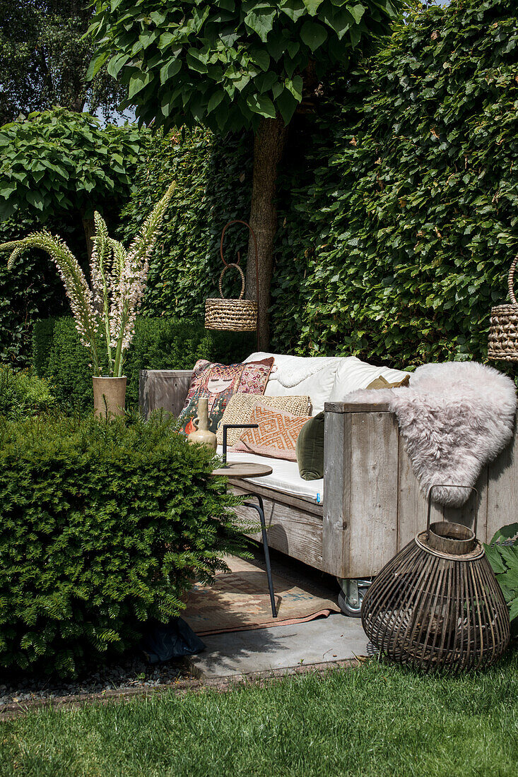 Wooden bench with cushions and furs in cozy garden corner