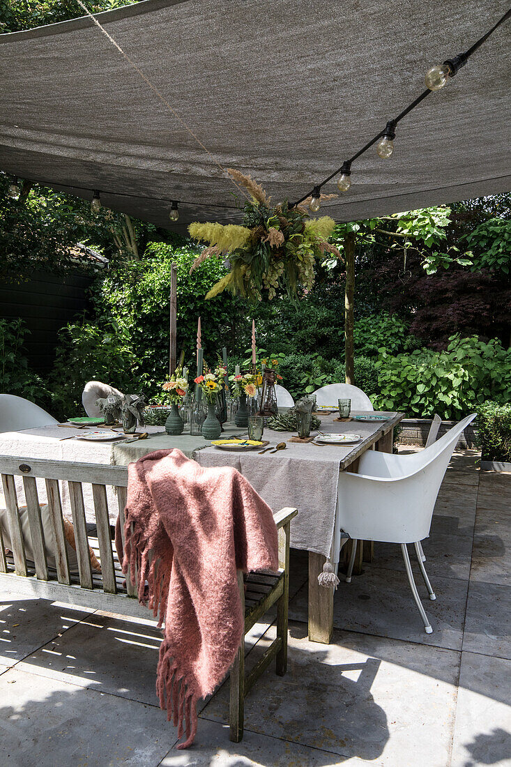 Laid garden table with fresh cut flowers under a sunshade with fairy lights