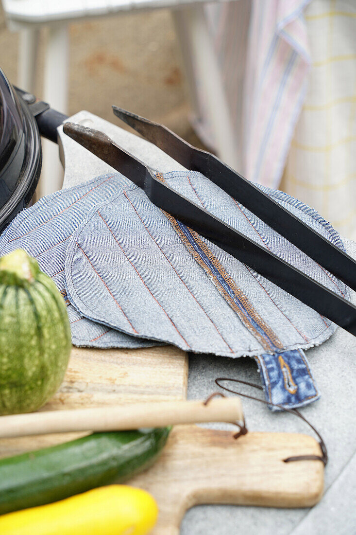 Selbstgemachte Topflappen aus Jeansstoff auf Holzbrett neben Gemüse