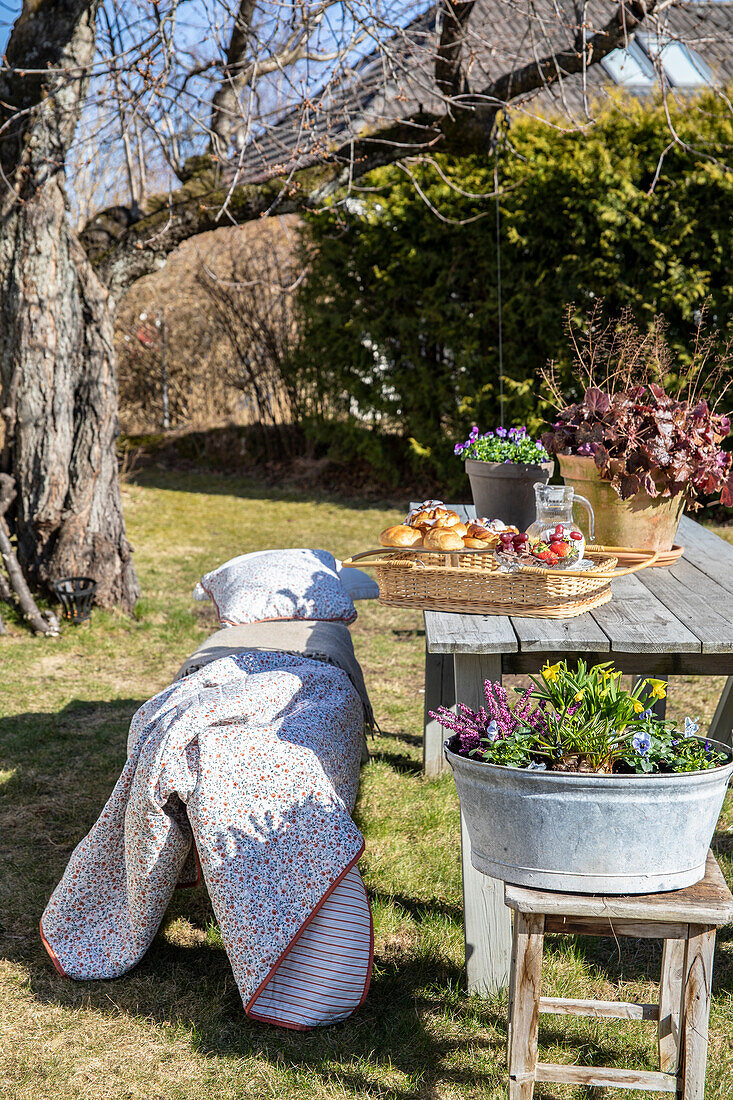 Frühlingspicknick mit Tablett auf Holztisch im Garten, Decke und Kissen