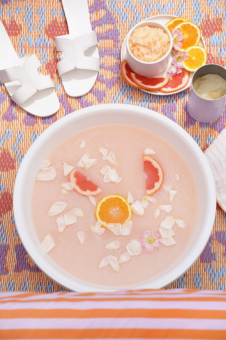 Fußbad mit Blütenblättern und Orangen- und Grapefruitscheiben auf buntem Teppich