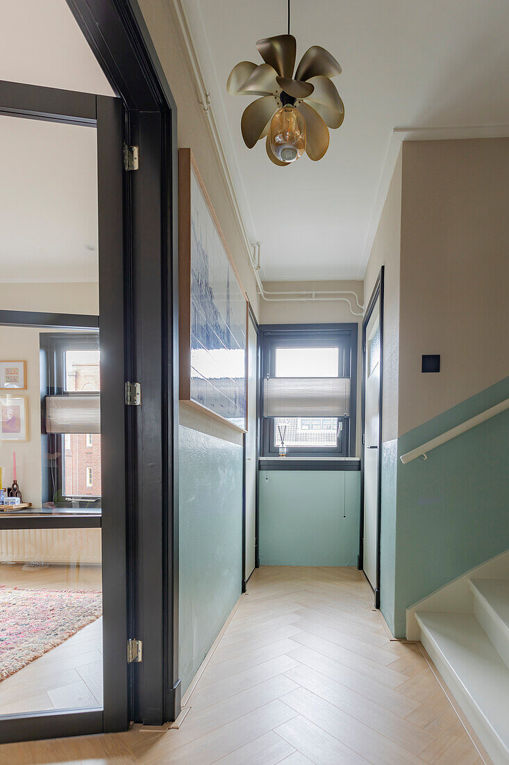 Hallway with light green wall color, herringbone parquet flooring and golden ceiling light