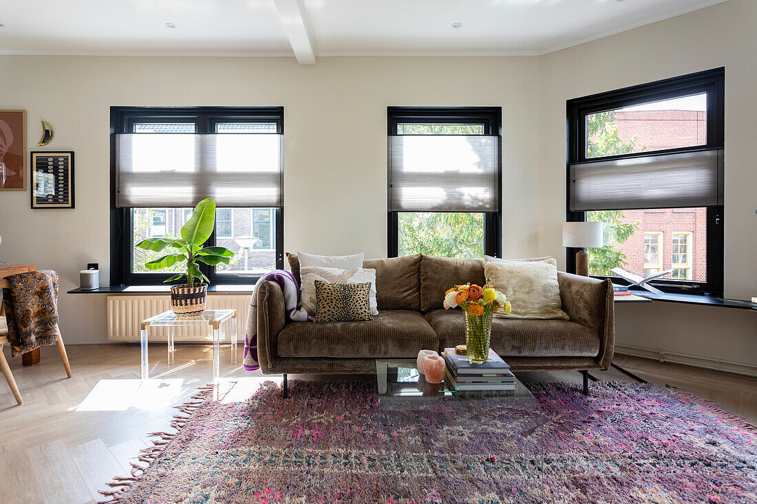 Living room with brown velvet sofa, patterned rug and large windows