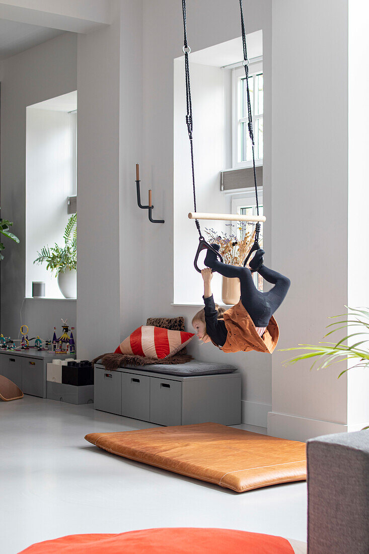 Child hangs on gymnastic rings in the living room