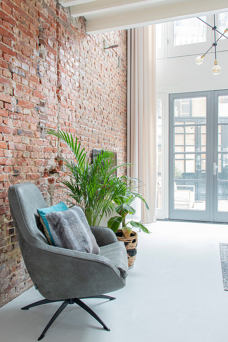 Cement floor and brick wall in modern living room with plants and grey armchair